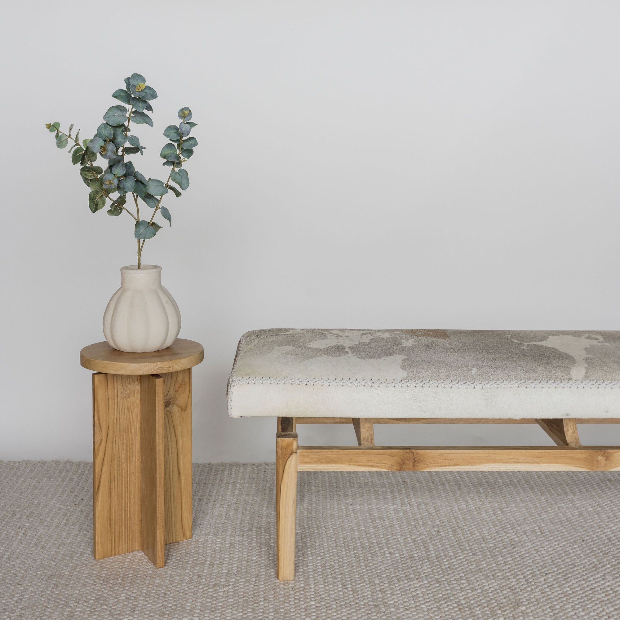 close up view of a mottled grey cowhide bench or ottoman next to a wooden side table