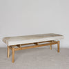 angled view of a dark cream cowhide ottoman bench on a teak wood base