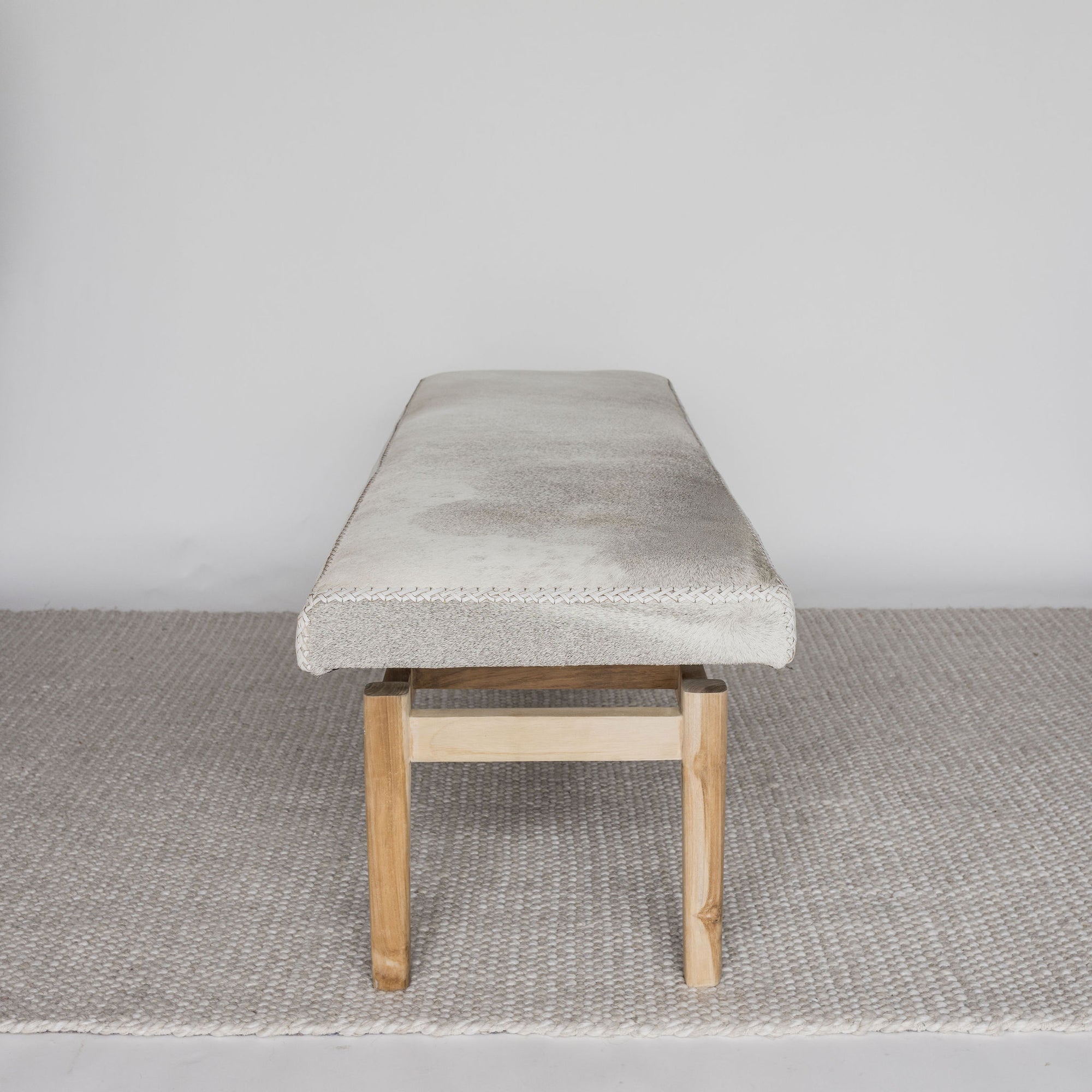 end view of the cream coloured cowhide ottoman bench on a teak wood base by corcovado 