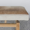 close up end view of Corcovado's cowhide ottoman bench which featuring caramel and cream shades on top of a looped rug.