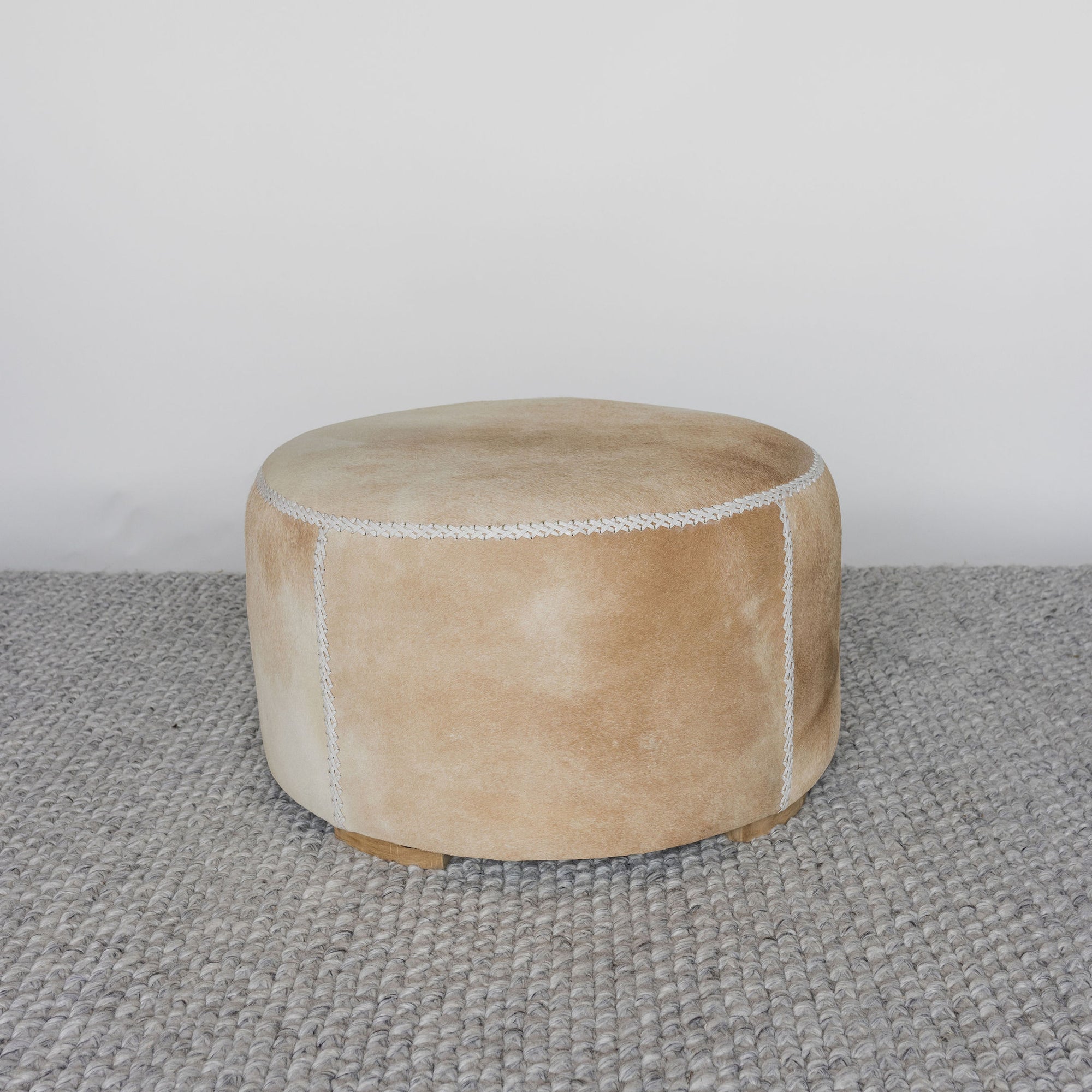 front view of a caramel coloured round cowhide ottoman coffee table by Corcovado 