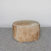 A caramel brown coloured round cowhide ottoman coffee table by Corcovado