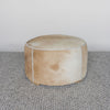 side view of the front view of a caramel coloured round cowhide ottoman coffee table by Corcovado