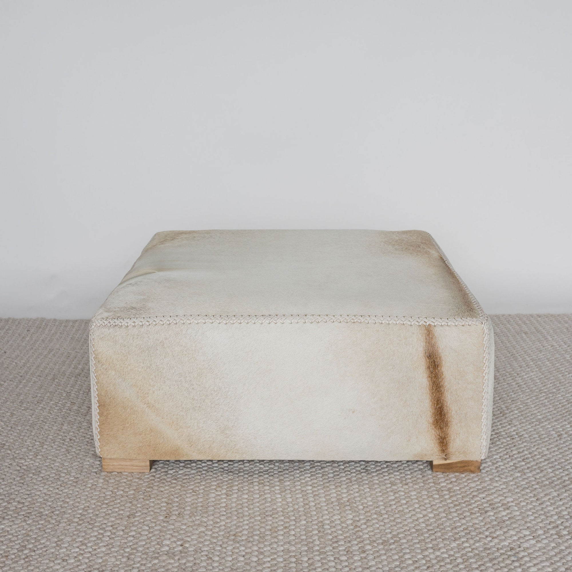 front view of the square cowhide ottoman coffee table showing the distinctive caramel coloured natural markings from the hide