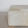 close up corner view of the square cowhide ottoman coffee table in neutral and cream tones