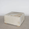 angled photo of the cream light coloured sqarae cowhide ottoman coffee table