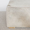 close up corner view of the square cowhide ottoman coffee table in natural tones, showing the leather braiding detail