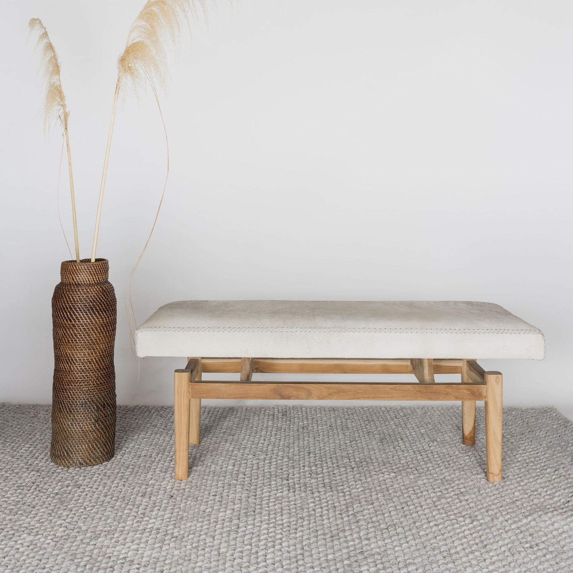 front view of a light coloured cream cowhide bench seat from corcovado next to a brown rattan basket 