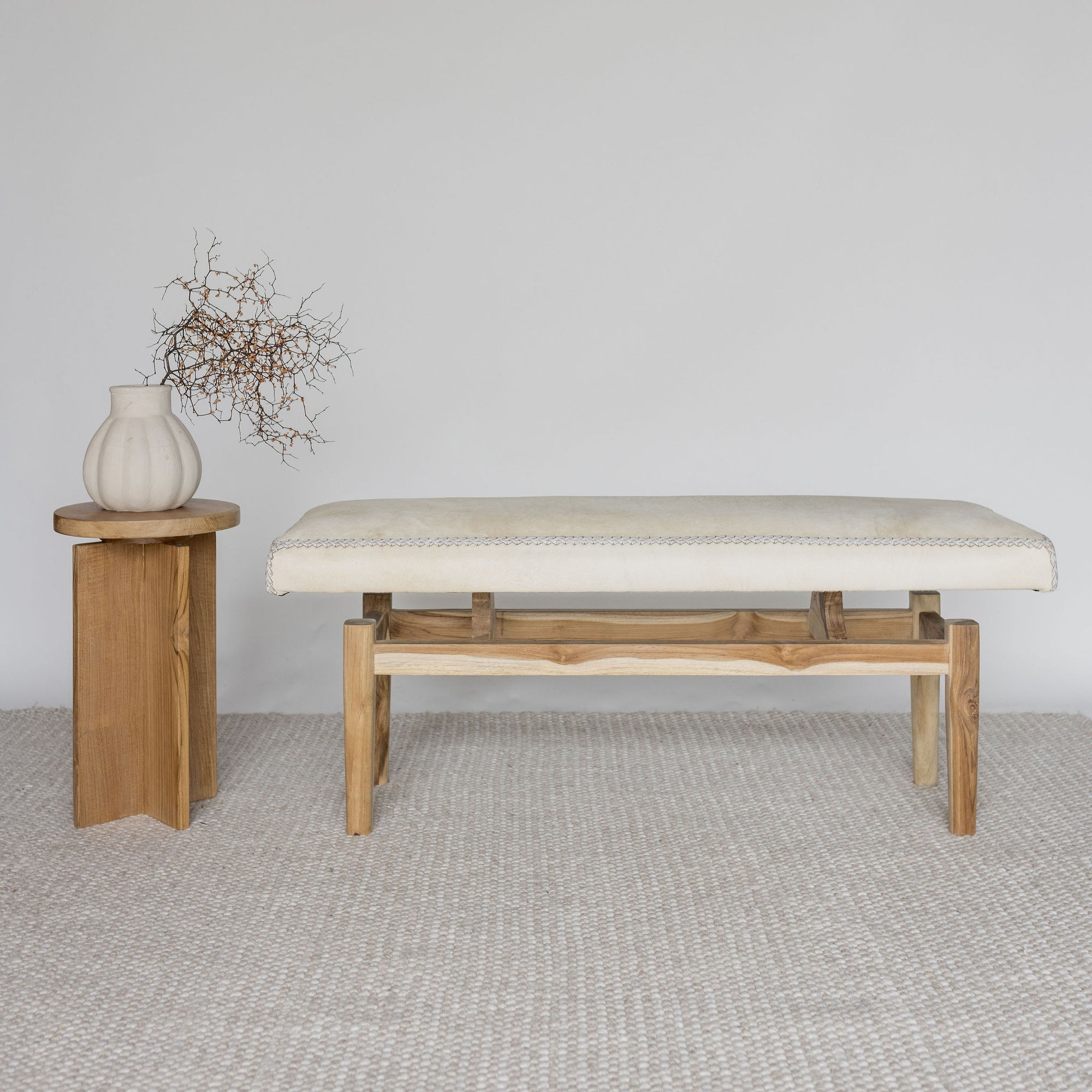 cream coloured cowhide ottoman bench seat next to a small wooden table 