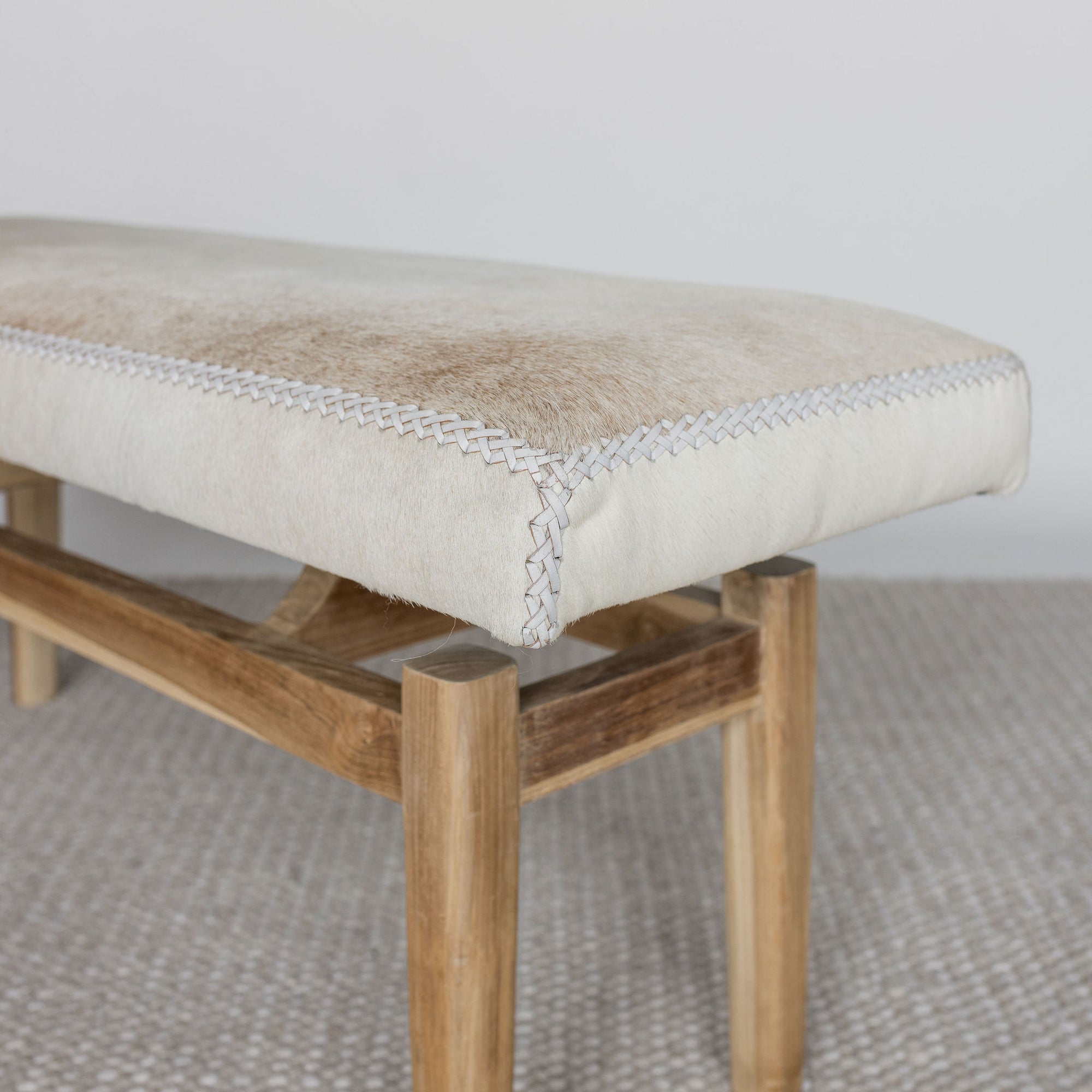 close up angled view of a cowhide bench seat in cream earthy neutral tones