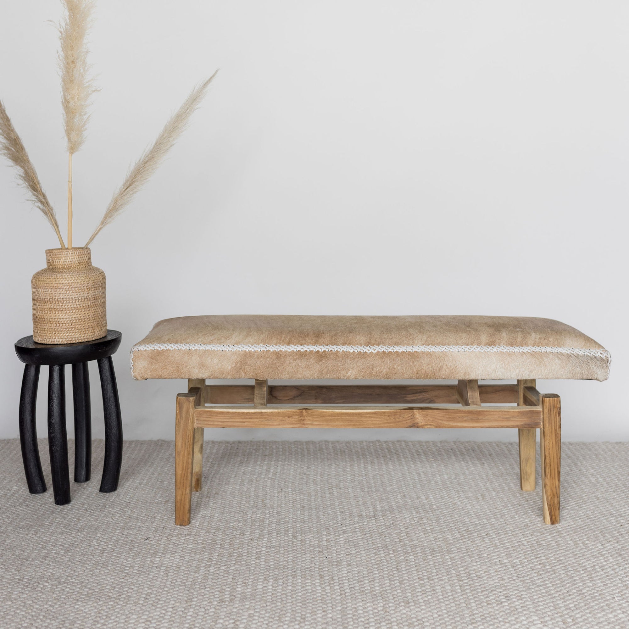 front view of a caramel brown and cream coloured cowhide bench seat next to a black side table and rattan basket