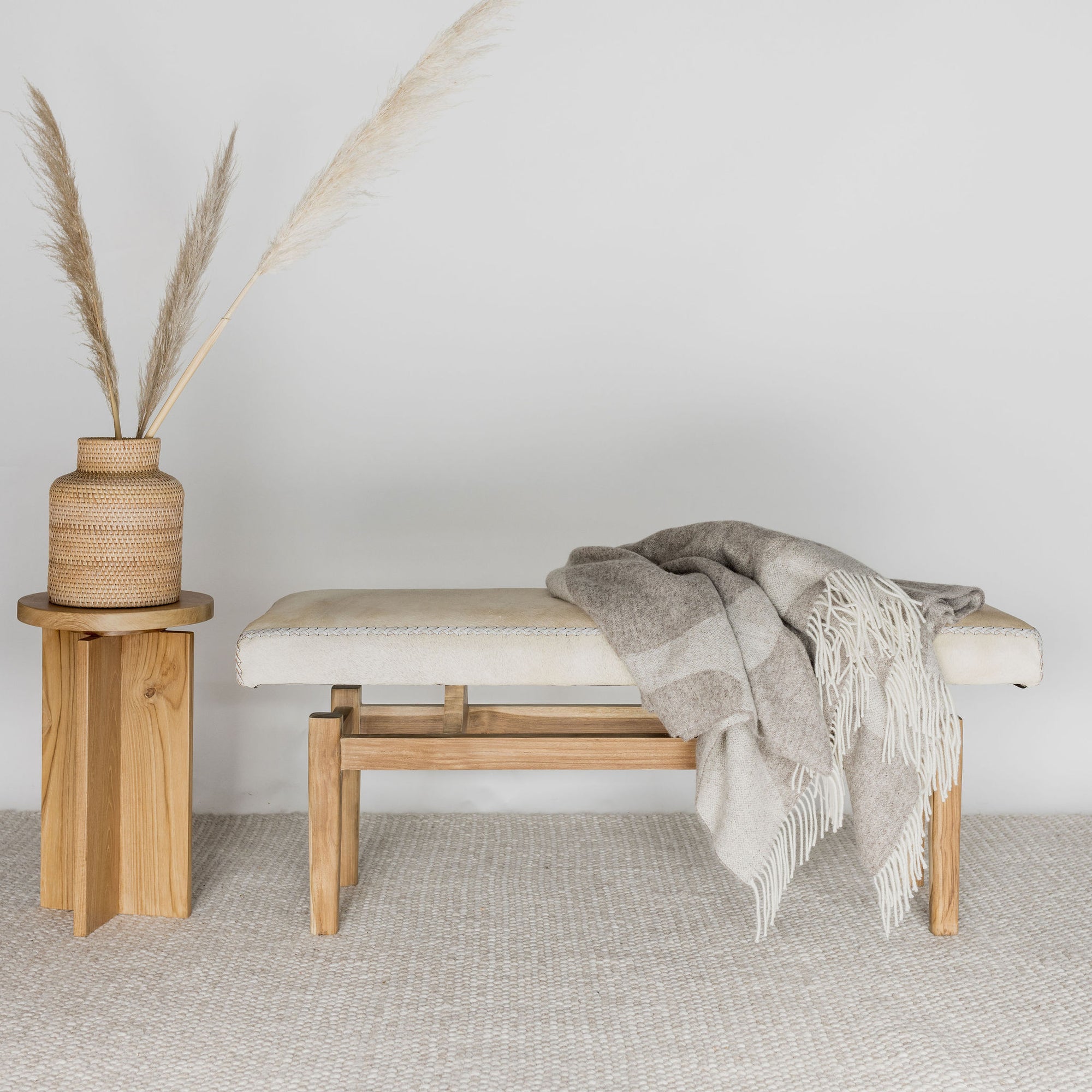 cream coloured cowhide bench seat ottoman next to a wooden side table 