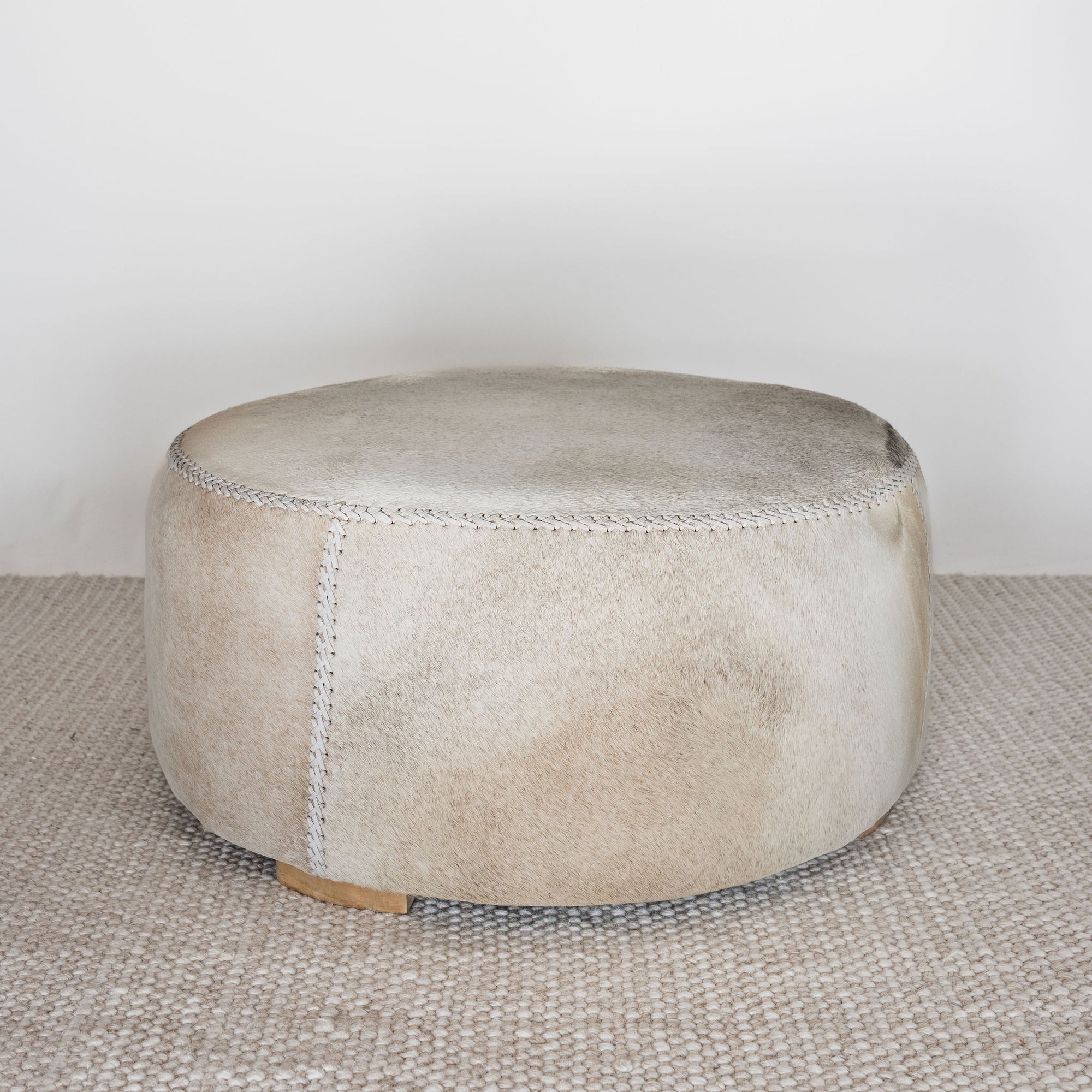 neutral toned natural cowhide ottoman coffee table that is round in shape