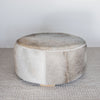 front view of a charcoal grey round cowhide ottoman coffee table