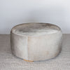 side view of a charcoal grey round cowhide ottoman coffee table