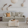 hale linen sofa with a hide square ottoman and a rattan bowl from corcovado  with 3 rustci handmade jugs holding faux foliage in shelves behind the sofa