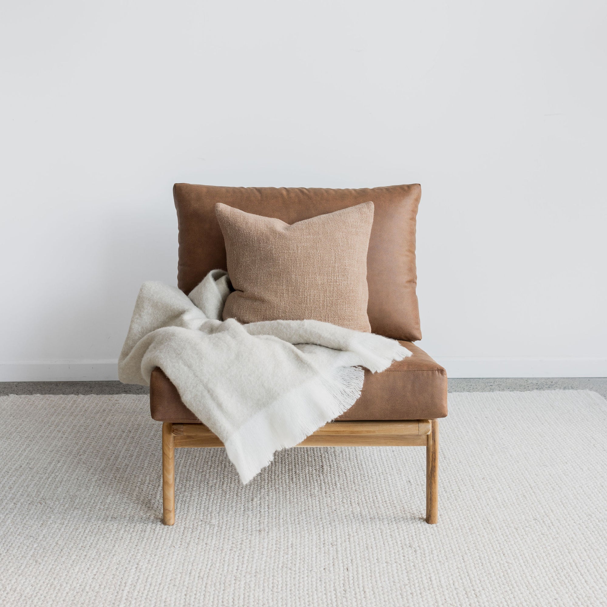 oversized lounge chair in tan leather like fabric with a cream throw blanket and a cushion