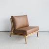 angled view of an oversized lounge chair in tan leather like fabric on a teak wood frame