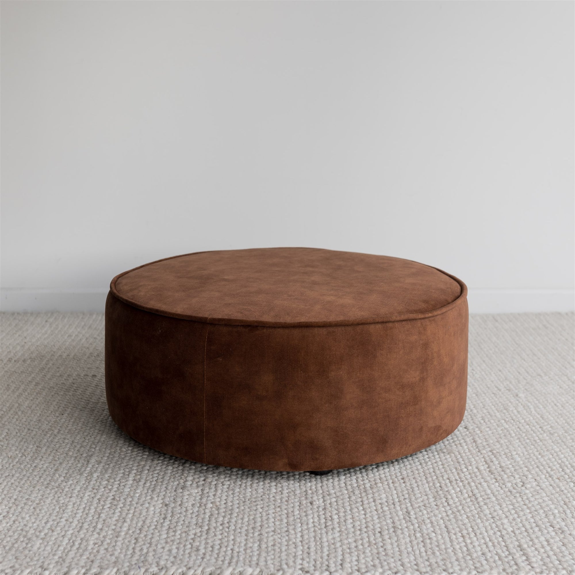 round velvet floor pouff or ottoman in a rich cinnamon colour with piped edging