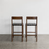 the back view of two serengeti bar stools with black woven leather seat and dark brown wood