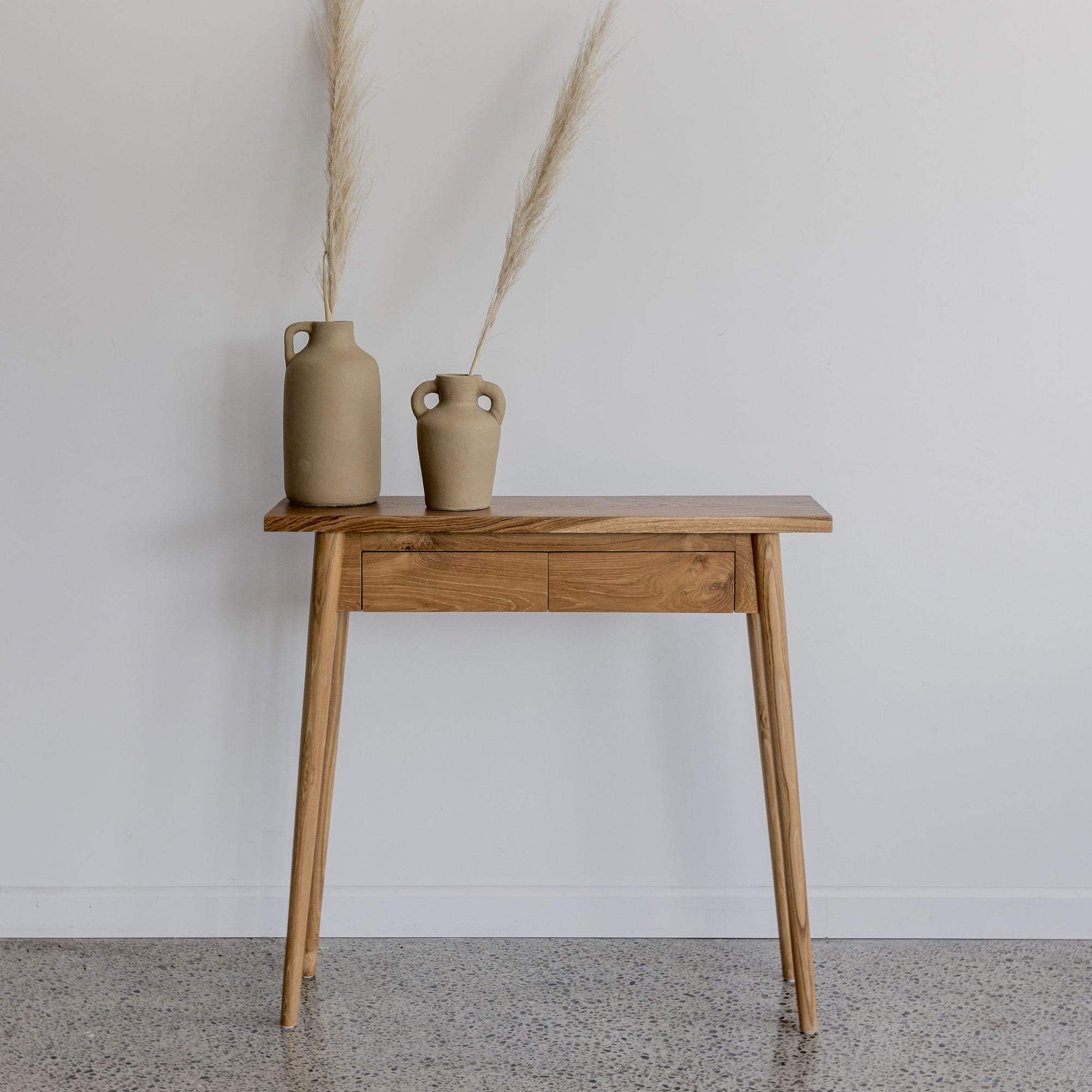 slim hallway console table in natural wood with two drawers and two brown vases displayed on top